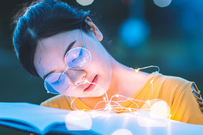 Close-up of young woman with illuminated string lights on book