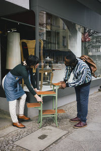 Female upcycling store owner showing furniture to male customer at sidewalk