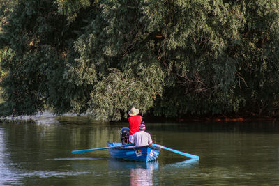 Rear view of men in boat on lake against trees