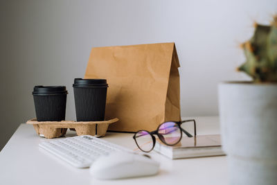 Package with food delivery and cups of coffee at workplace, glasses and notepad with keyboard