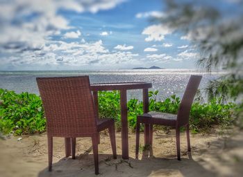 Empty chairs on beach against sky