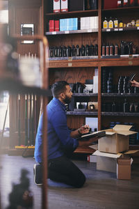 Salesman kneeling while looking at beauty product being held by colleague in deli