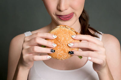 Midsection of woman holding burger against gray background