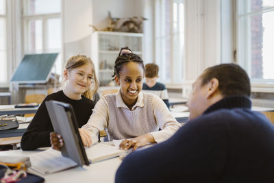 Smiling schoolgirl showing tablet pc to male teacher in classroom