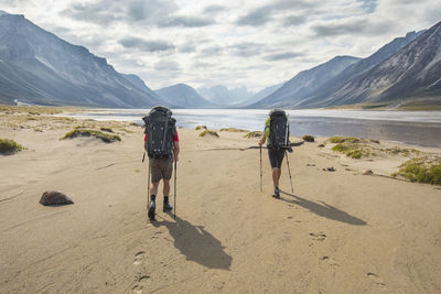 Rear view of two backpackers hiking, leaving footprints in the sand.