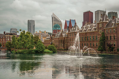 Modern buildings by river against sky in city