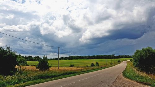 Empty road amidst field against sky