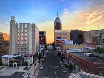 City street amidst buildings against sky during sunset