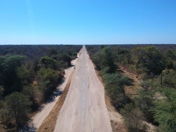 Road amidst trees against clear blue sky