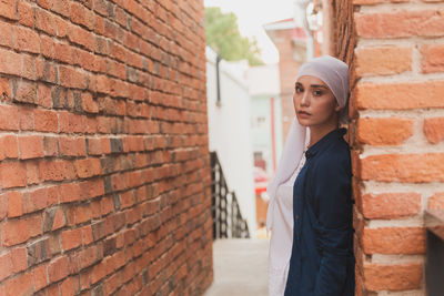 Portrait of young woman standing by brick wall