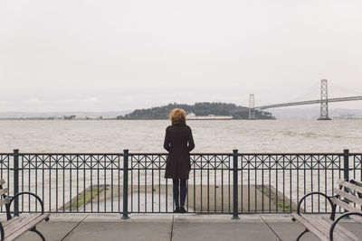 Rear view of woman standing on suspension bridge over sea against sky