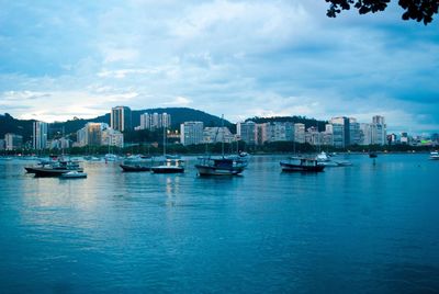 Boats in sea by cityscape against sky