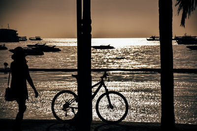 Silhouette people on street by sea against sky