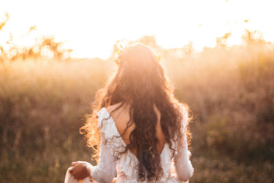 Rear view of woman standing on field against sky during sunset