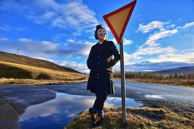 Mid adult woman standing by road sign against puddle with reflection