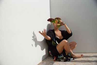 Young woman sitting on table against wall