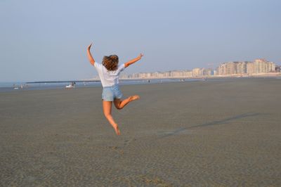 Rear view of man jumping on beach against clear sky