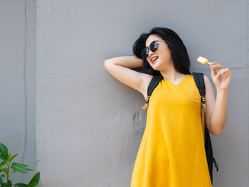 Young woman standing against yellow wall