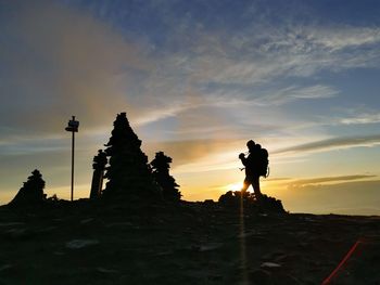 Silhouette man photographing on mountain against sky during sunset