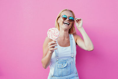 Smiling woman holding lollipop against pink background