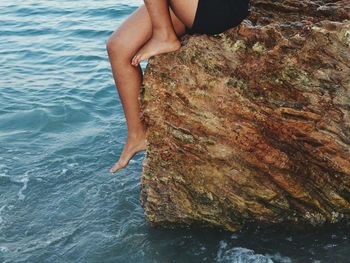 Low section of person sitting on rock in sea