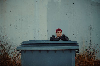 Portrait of young woman leaning on container against concrete wall