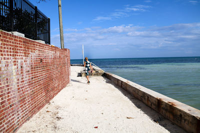 Rear view of woman walking at promenade by sea against sky