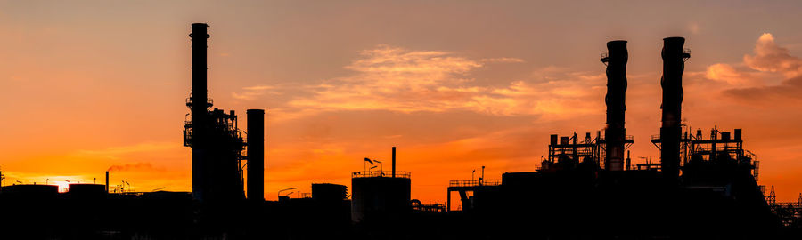 Silhouette factory against sky during sunset