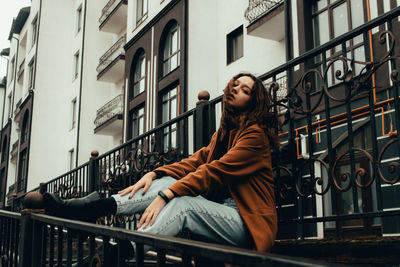 Young woman looking away while sitting on railing