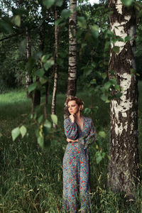 Woman standing by tree trunk in forest