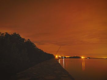 Illuminated trees by sea against sky during sunset