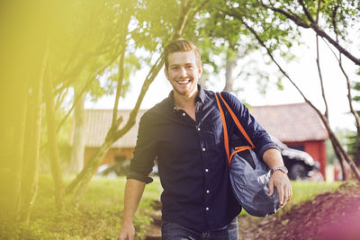 Portrait of smiling man carrying luggage on steps at back yard