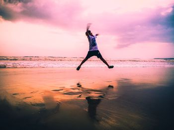 Silhouette woman jumping on beach against sky during sunset