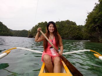 Portrait of smiling woman sitting outrigger at river 