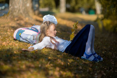 Side view of girl with backpack lying on grassy field in park during autumn