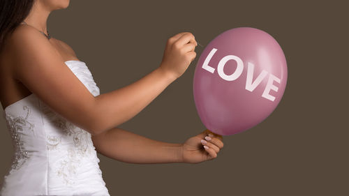 Midsection of bride holding balloon and needle against brown background