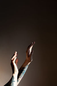Low angle view of tattooed woman's hands against dark background