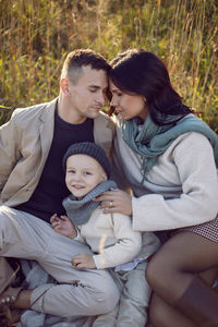 Family of three people mom, dad, son are sitting on the field in autumn