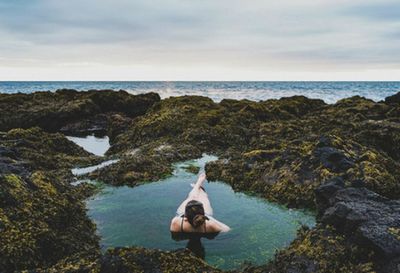 Man standing on rock by sea against sky