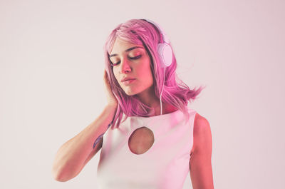 Close-up of girl wearing headphones against pink background