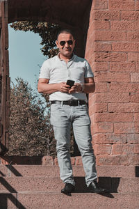 Man using smart phone standing against brick wall