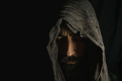 Face of a young man covering his face with a dark scarf on a black background