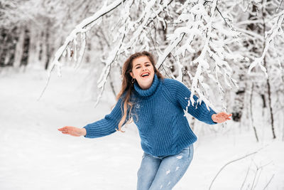 Happy young woman with arms raised in snow