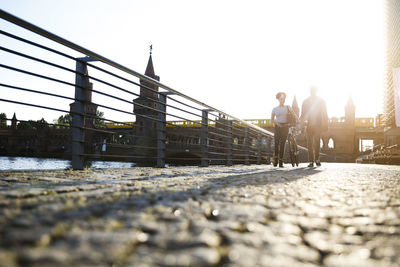 Couple walking by river, pushing bicycle