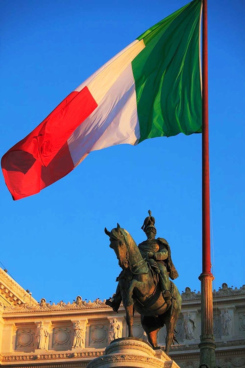 low angle view, clear sky, flag, patriotism, architecture, sculpture, built structure, identity, blue, statue, famous place, building exterior, art, national flag, travel, art and craft, travel destinations, human representation, tourism, creativity