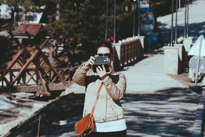 Man photographing woman with umbrella standing at camera