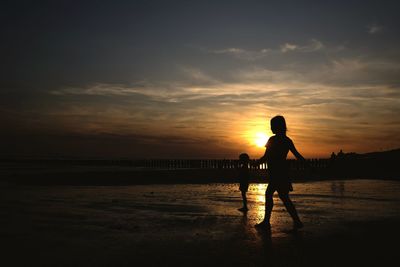 Silhouette men standing on beach against sky during sunset