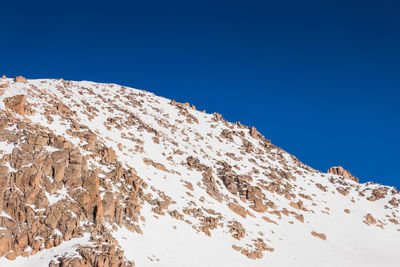 Low angle view of snowcapped mountain against clear blue sky