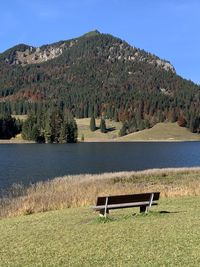 Bench in park by lake against sky