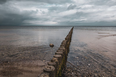 Wooden posts on sea against sky